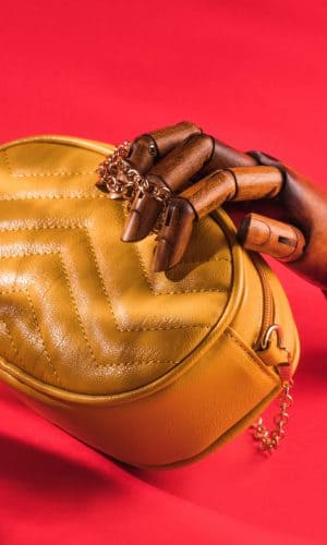 wooden-hand-holding-yellow-eco-leather-bag-on-red-background-female-fashion-accessories-handbag_t20_ZY2dpn